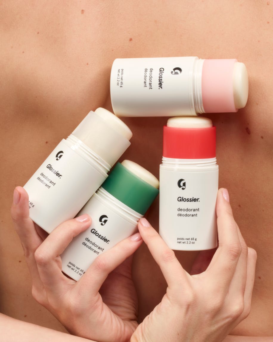 model holding all four scents of Glossier Deodorant